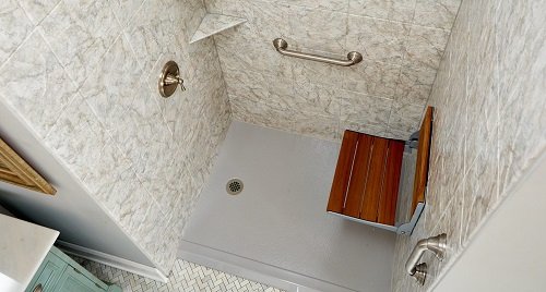 The inside a of no-threshold shower enclosure with grab bars and a bench seat. 